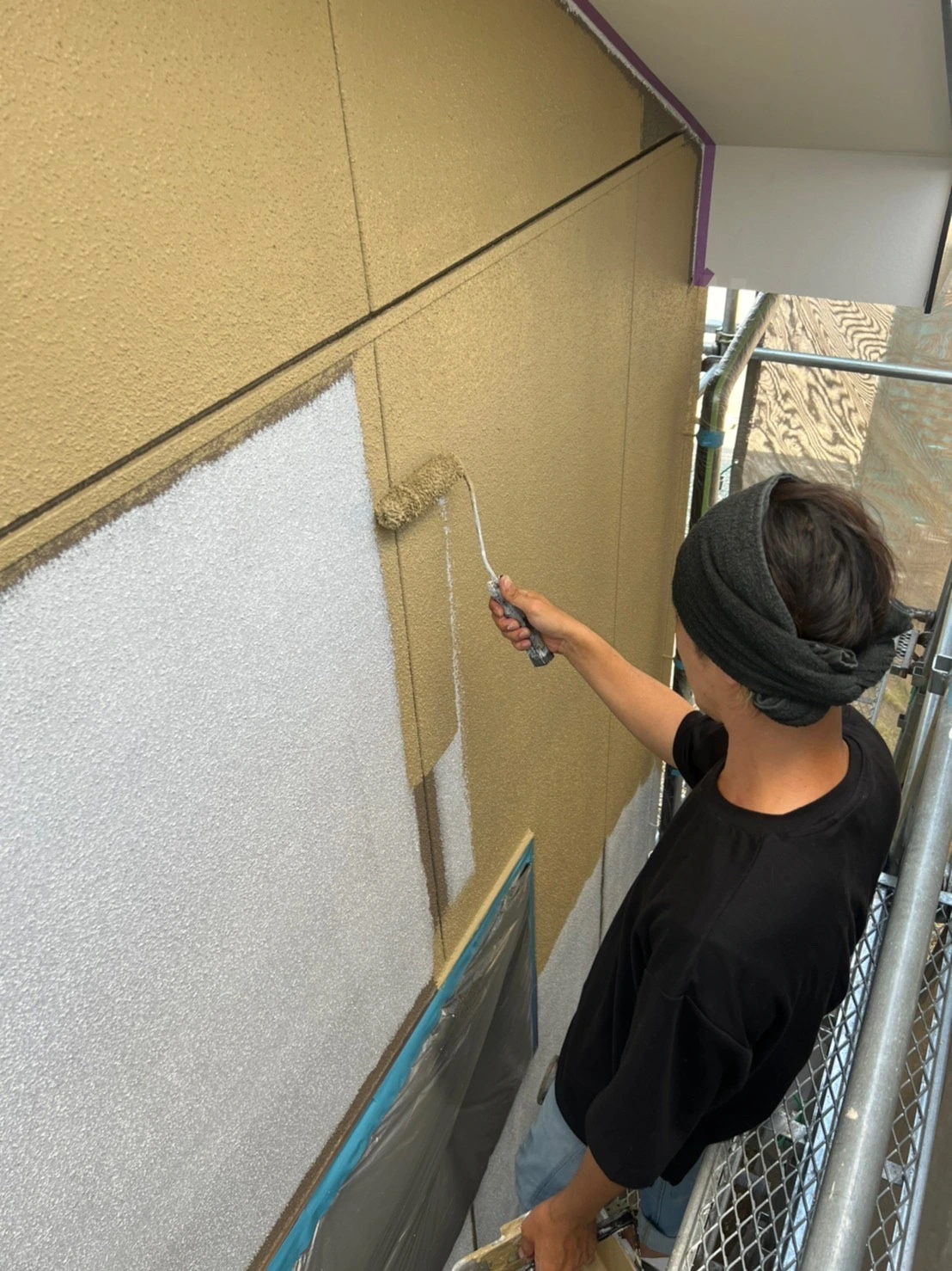 足場の上で外壁をローラー塗装する作業員